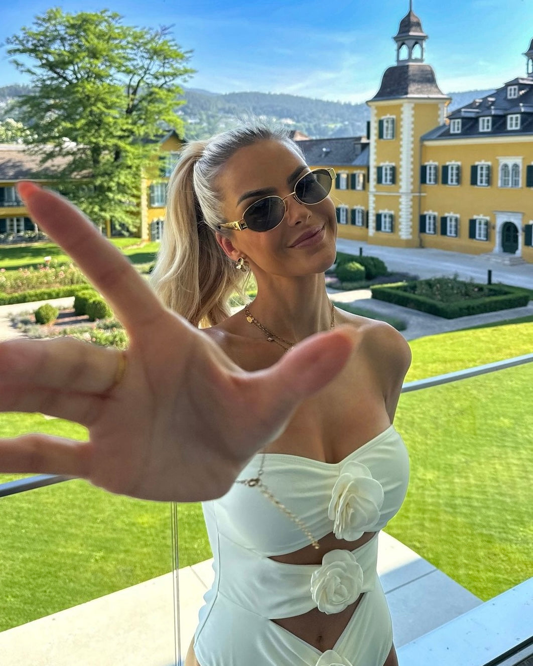 Adriana Flower Swimsuit, a bandeau one-piece featuring three sculpted rosette accents and strategic front cutouts. Supportive stretch swim fabric and a high-leg silhouette create a smooth, waist-defining, photo-ready look for beach or resort.