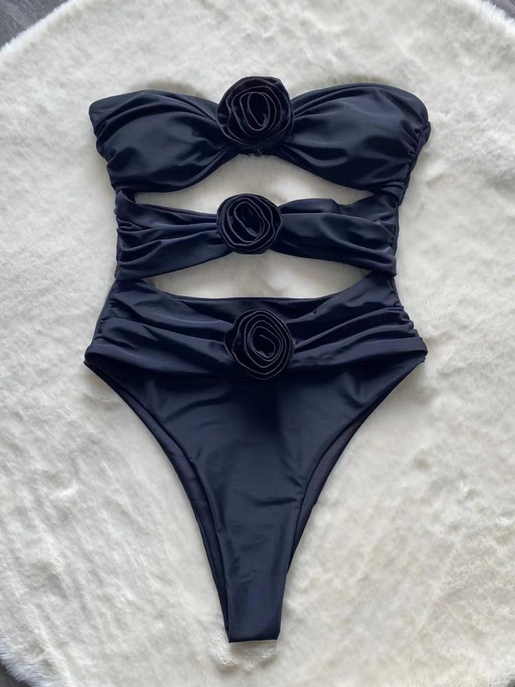 Adriana Flower Swimsuit, a bandeau one-piece featuring three sculpted rosette accents and strategic front cutouts. Supportive stretch swim fabric and a high-leg silhouette create a smooth, waist-defining, photo-ready look for beach or resort.