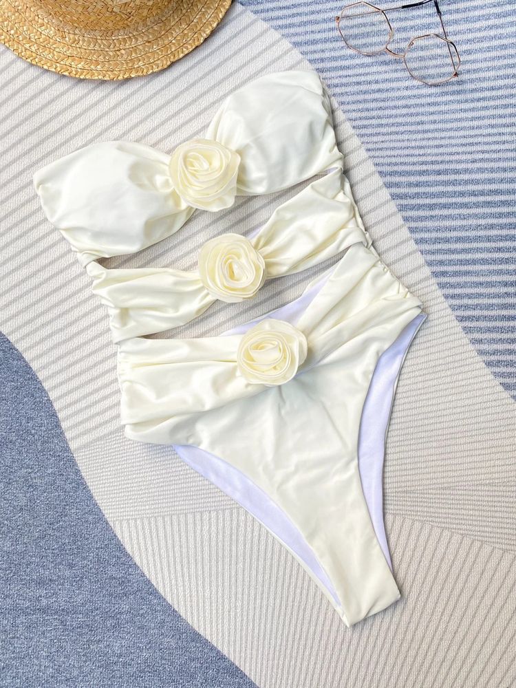 Adriana Flower Swimsuit, a bandeau one-piece featuring three sculpted rosette accents and strategic front cutouts. Supportive stretch swim fabric and a high-leg silhouette create a smooth, waist-defining, photo-ready look for beach or resort.