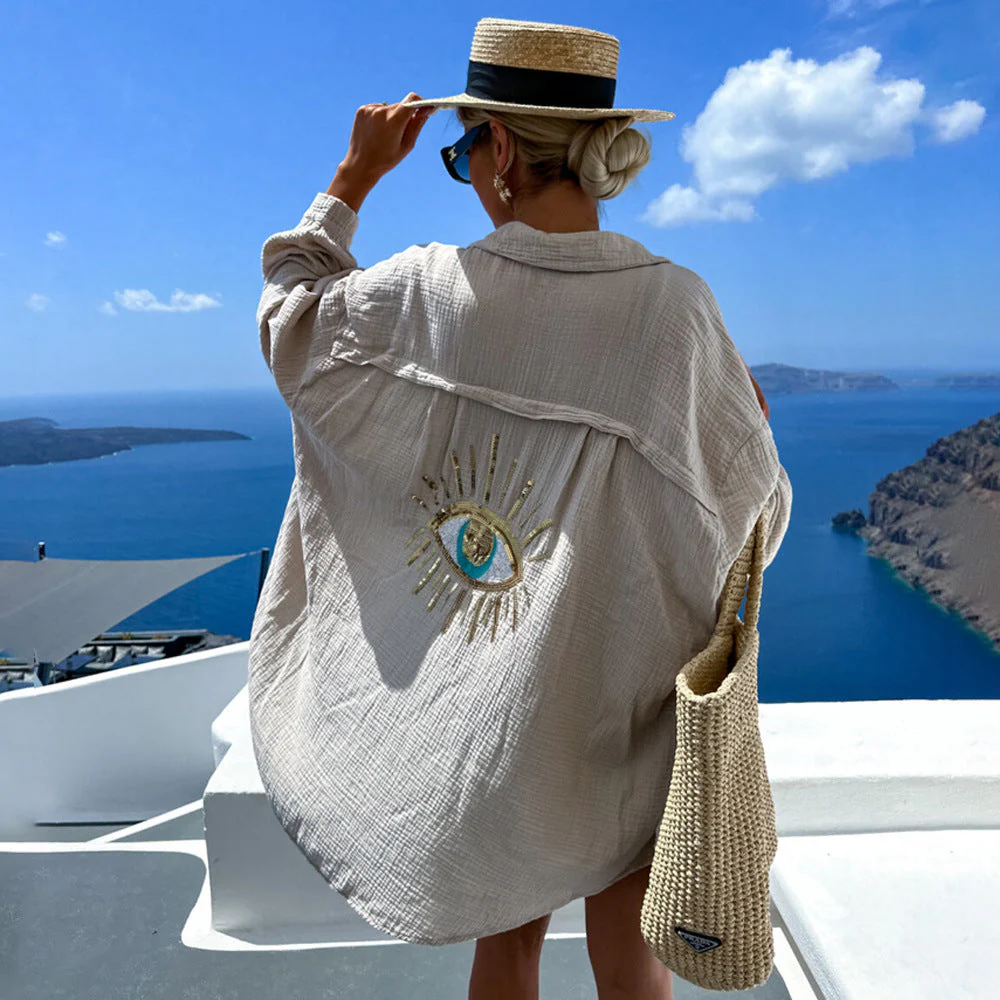 Aisling eye-catching blouse, an oversized button-up with lightweight crinkled texture and shimmering sequin-and-bead evil-eye motif on the back; relaxed drop-shoulder fit in black or white, ideal as a beach coverup or for casual chic layers.
