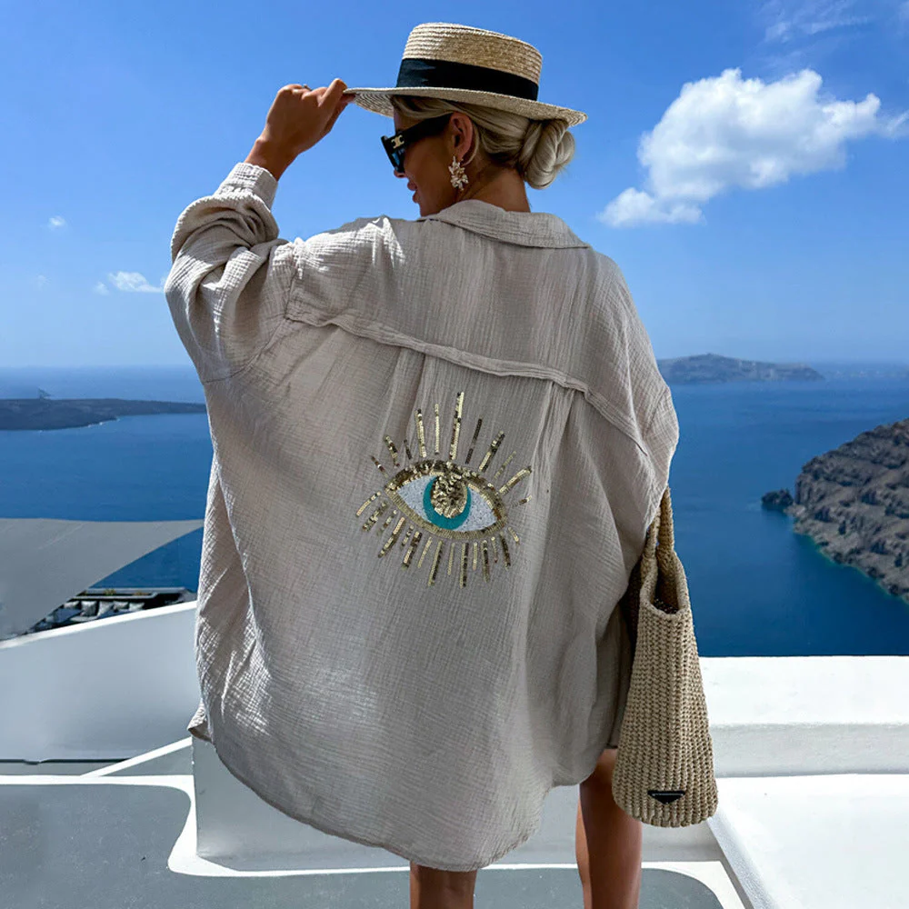 Aisling eye-catching blouse, an oversized button-up with lightweight crinkled texture and shimmering sequin-and-bead evil-eye motif on the back; relaxed drop-shoulder fit in black or white, ideal as a beach coverup or for casual chic layers.