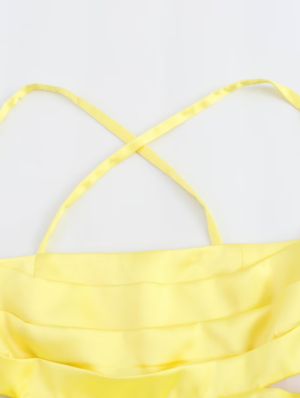 Amalfi Satin Mini Dress in lemon yellow with structured pleated bandeau bodice, adjustable thin straps, open back with criss-cross ties and a flared double-layered skirt. Polyester satin offers fluid movement for parties, vacations and seaside events.