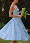 Ariana Sleeveless Midi Sundress in blue-cream gingham with a square neckline, wide straps and a fitted bodice trimmed with ribbon eyelets. Gathered midi skirt with side patch pockets and back zipper; chic and versatile for daytime events.