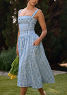 Ariana Sleeveless Midi Sundress in blue-cream gingham with a square neckline, wide straps and a fitted bodice trimmed with ribbon eyelets. Gathered midi skirt with side patch pockets and back zipper; chic and versatile for daytime events.