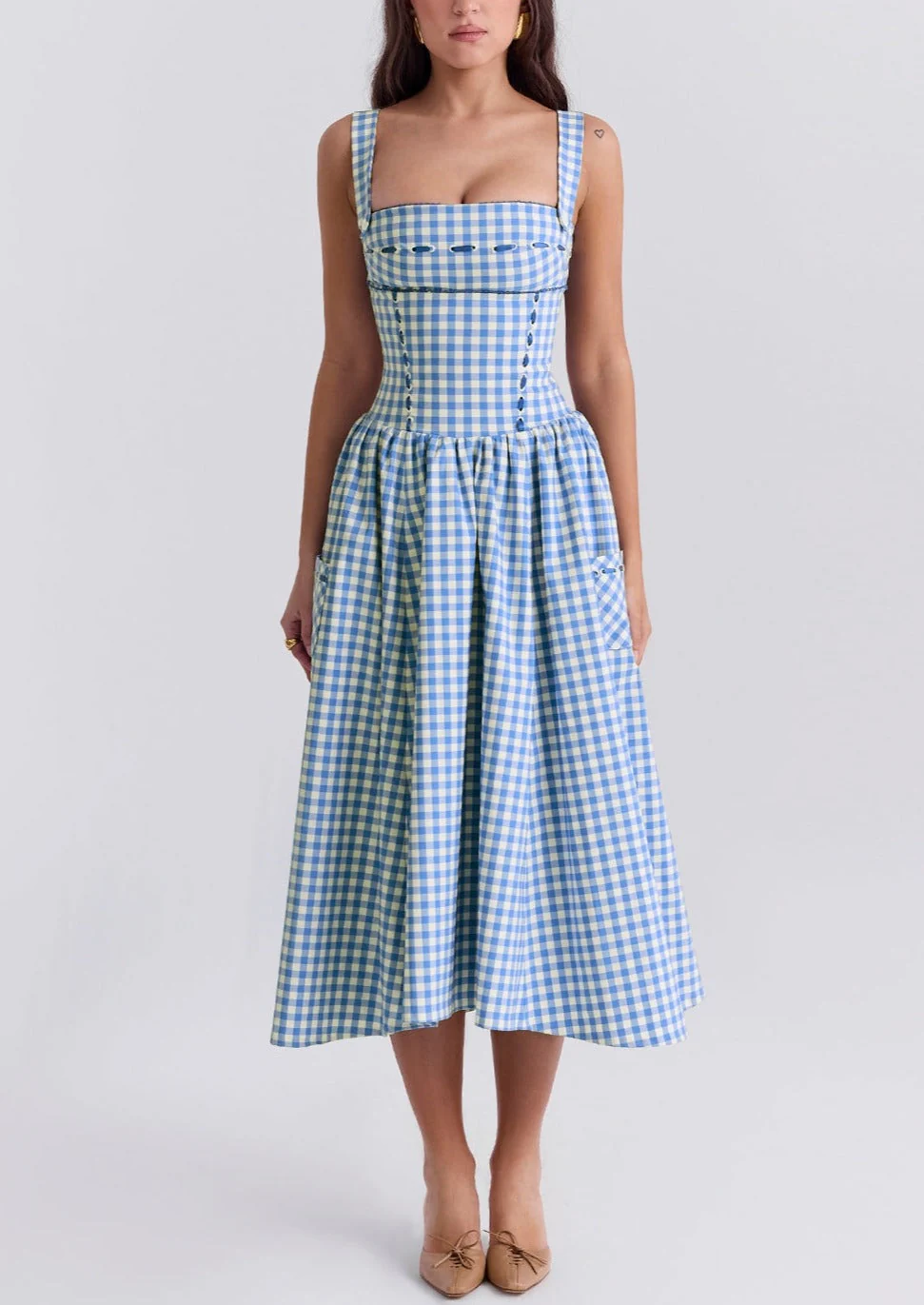 Ariana Sleeveless Midi Sundress in blue-cream gingham with a square neckline, wide straps and a fitted bodice trimmed with ribbon eyelets. Gathered midi skirt with side patch pockets and back zipper; chic and versatile for daytime events.