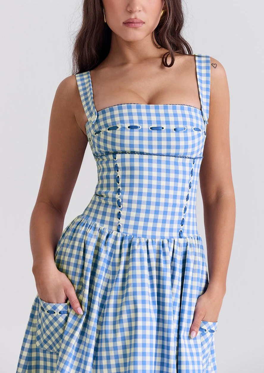 Ariana Sleeveless Midi Sundress in blue-cream gingham with a square neckline, wide straps and a fitted bodice trimmed with ribbon eyelets. Gathered midi skirt with side patch pockets and back zipper; chic and versatile for daytime events.