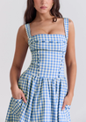Ariana Sleeveless Midi Sundress in blue-cream gingham with a square neckline, wide straps and a fitted bodice trimmed with ribbon eyelets. Gathered midi skirt with side patch pockets and back zipper; chic and versatile for daytime events.