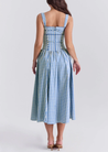 Ariana Sleeveless Midi Sundress in blue-cream gingham with a square neckline, wide straps and a fitted bodice trimmed with ribbon eyelets. Gathered midi skirt with side patch pockets and back zipper; chic and versatile for daytime events.