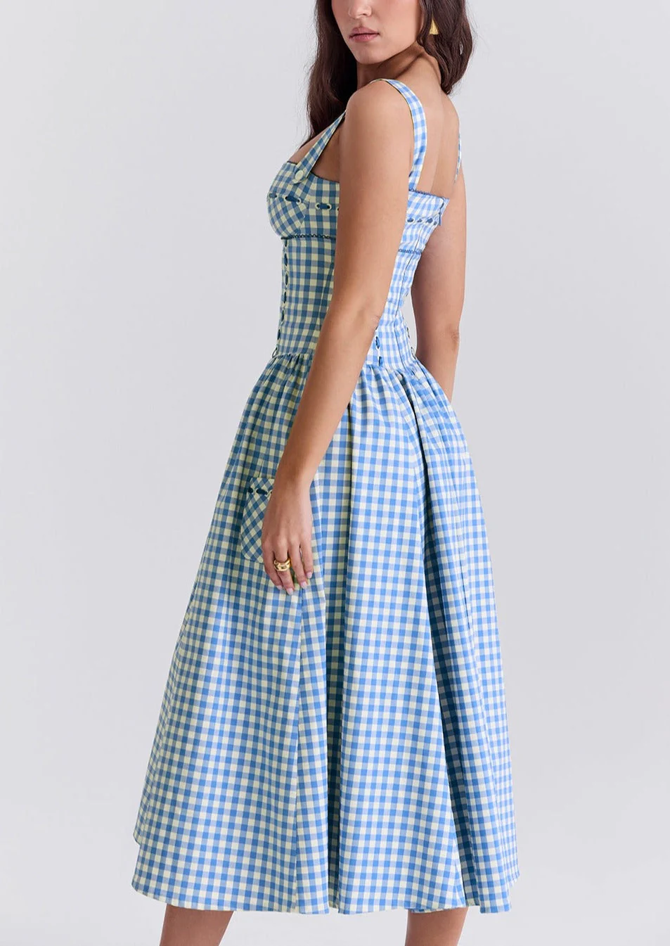 Ariana Sleeveless Midi Sundress in blue-cream gingham with a square neckline, wide straps and a fitted bodice trimmed with ribbon eyelets. Gathered midi skirt with side patch pockets and back zipper; chic and versatile for daytime events.