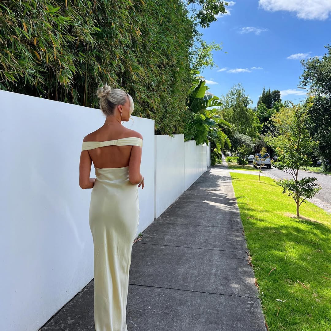 Emory satin backless maxi dress featuring an off-shoulder band, soft twist at the bust, and a sleek, body-skimming silhouette that falls to the floor. Lightweight satin with a refined sheen—ideal for weddings, formal dinners, and elegant evening events.