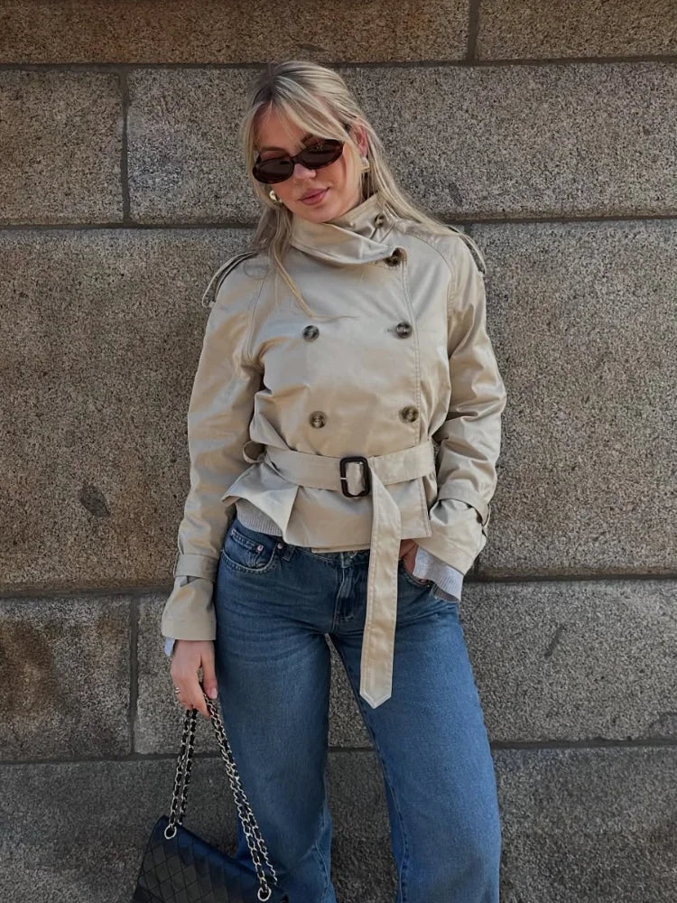 Isabelle high-neck belted trench coat in premium cotton blend with structured stand collar, double-breasted buttons, epaulettes and adjustable cuffs. Tailored silhouette layers over dresses, denim or trousers for refined autumn-winter style.