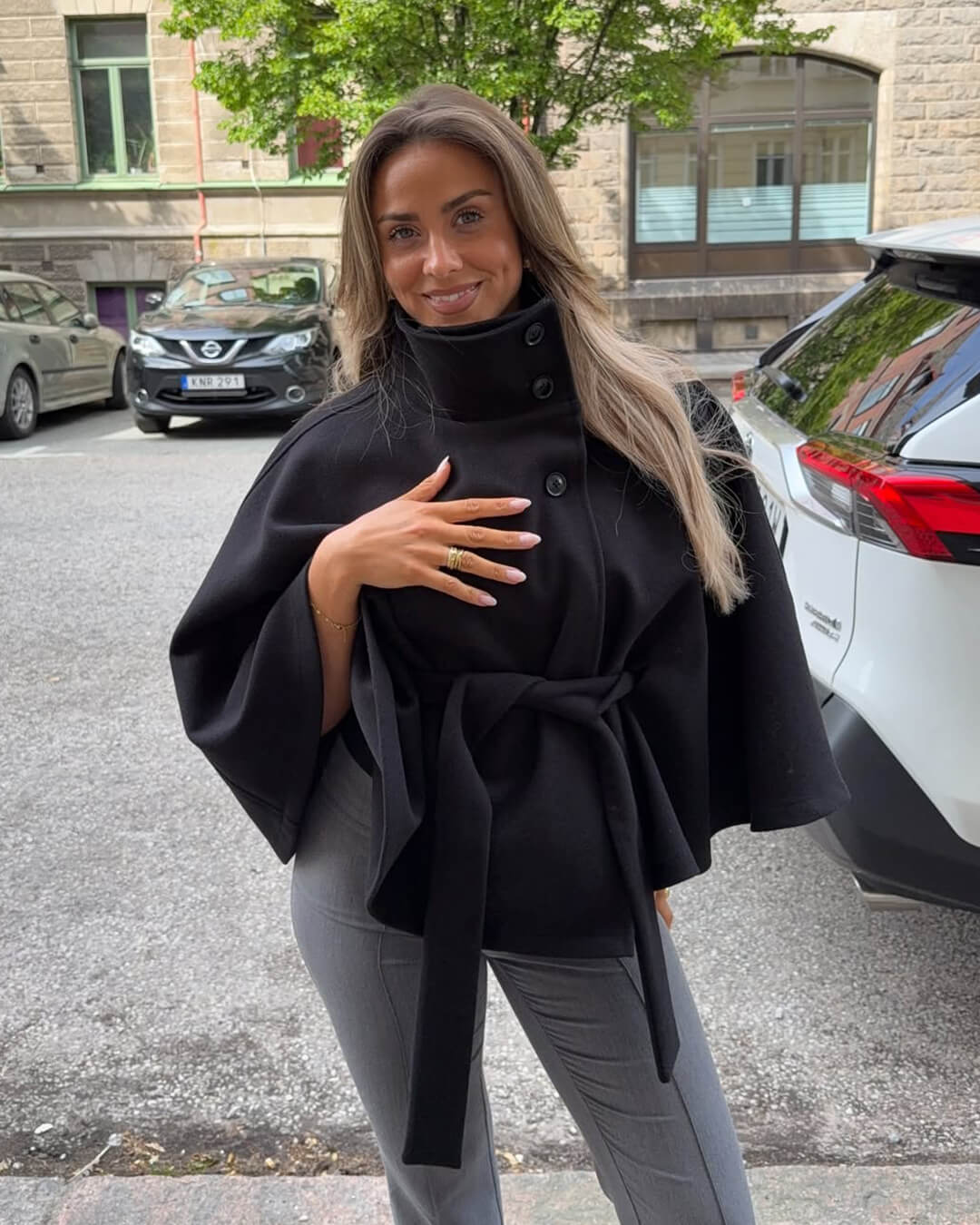 High-neck belted cape jacket in camel wool blend with buttoned collar, cape silhouette and waist-defining tie belt. Soft, warm and comfortable layering piece for autumn and winter, styled over knits or dresses for timeless elegance.