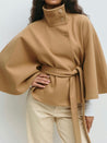 High-neck belted cape jacket in camel wool blend with buttoned collar, cape silhouette and waist-defining tie belt. Soft, warm and comfortable layering piece for autumn and winter, styled over knits or dresses for timeless elegance.