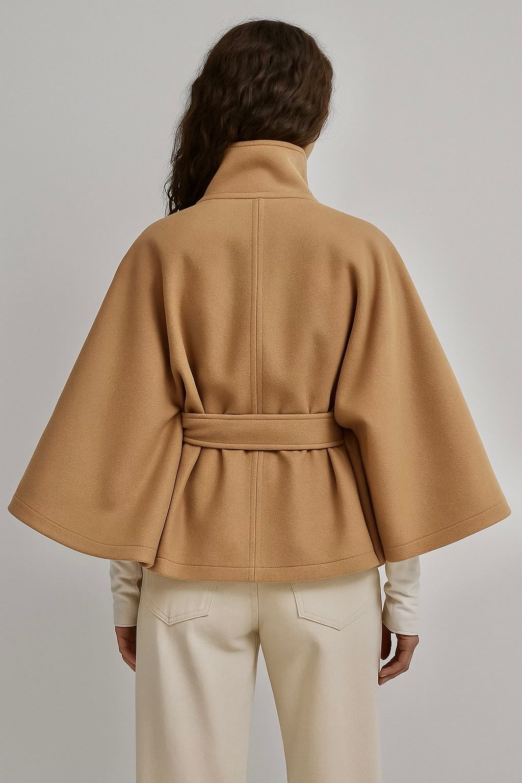 High-neck belted cape jacket in camel wool blend with buttoned collar, cape silhouette and waist-defining tie belt. Soft, warm and comfortable layering piece for autumn and winter, styled over knits or dresses for timeless elegance.