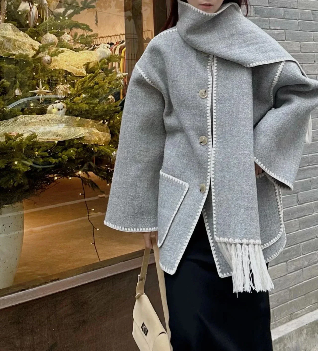 Vintage-inspired jacket in black or grey featuring an integrated scarf with fringe, contrast whipstitch edging, button front and large patch pockets. Relaxed straight silhouette in soft-touch fabric for cozy, stylish layering in cooler weather.