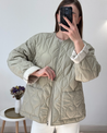Soft beige quilted oversized jacket featuring wave-pattern stitching, rounded neckline, full front zip and two roomy front pockets. Polyester shell with lightweight fibre fill provides warmth without bulk and a relaxed drape for easy layering in cooler seasons.