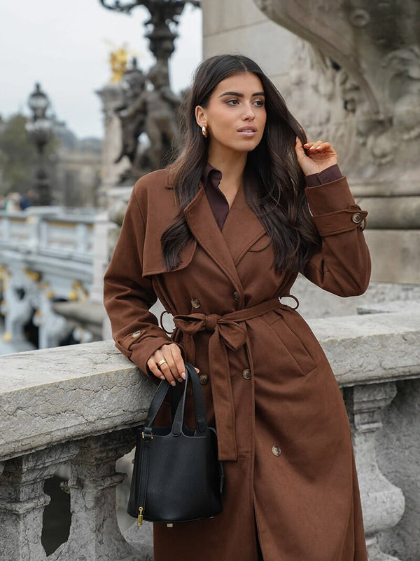 Molly faux suede trenchcoat featuring a velvety-soft finish, relaxed longline silhouette, buttoned front and waist-defining tie belt. Drapes comfortably over knits or dresses, adding refined, feminine style for transitional weather.