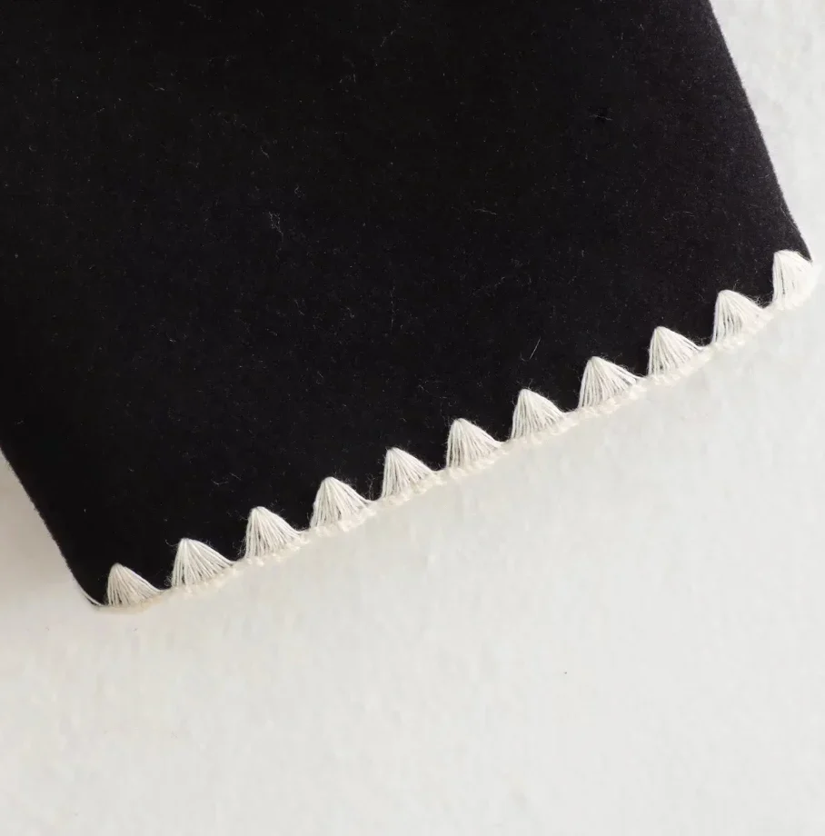 Nellie black wool-blend cape coat featuring a flowing silhouette with white contrast trim, front button fastening, practical side pockets and an attached oversized scarf collar. Warm, elegant outer layer that drapes over denim, knitwear or evening looks.