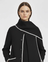 Nellie black wool-blend cape coat featuring a flowing silhouette with white contrast trim, front button fastening, practical side pockets and an attached oversized scarf collar. Warm, elegant outer layer that drapes over denim, knitwear or evening looks.
