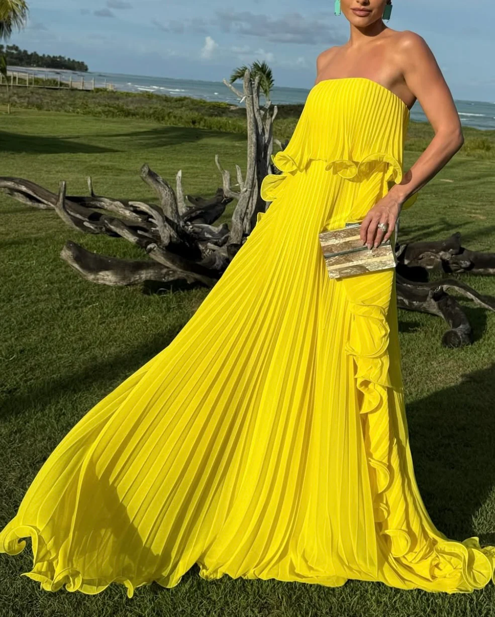 Ravello strapless pleated maxi dress featuring a layered flounce bodice, vertical knife pleats, and cascading side ruffles. Lightweight polyester drape lengthens the silhouette with elegant motion—perfect for weddings, garden parties, and evening events.
